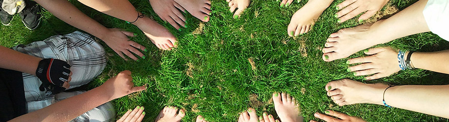 Viele nackte Hände und Füße bilden auf einer grünen Wiese einen Kreis.