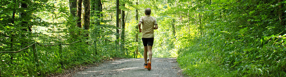 Ein sportlicher Mann joggt mitten in einem grünen Wald.