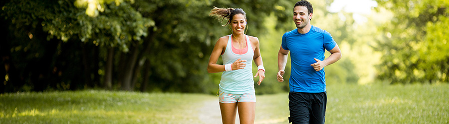 Ein sportliche Frau und ein sportlicher Mann joggen fröhlich durch einen Wald.