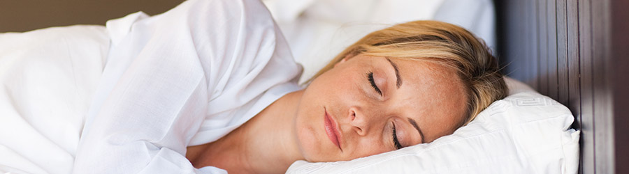 Eine junge blonde Frau schläft in einem weichem Bett.