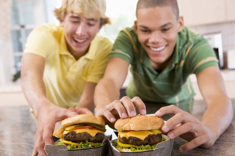Zwei jugendlich hungrige Teenager greifen nach einem saftigen Cheeseburger in einer Verpackung.